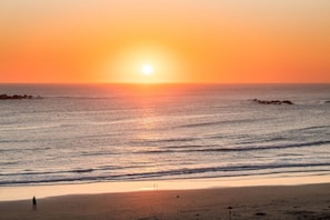 A beach with a sunset, calm sea, and a person standing on the shore.