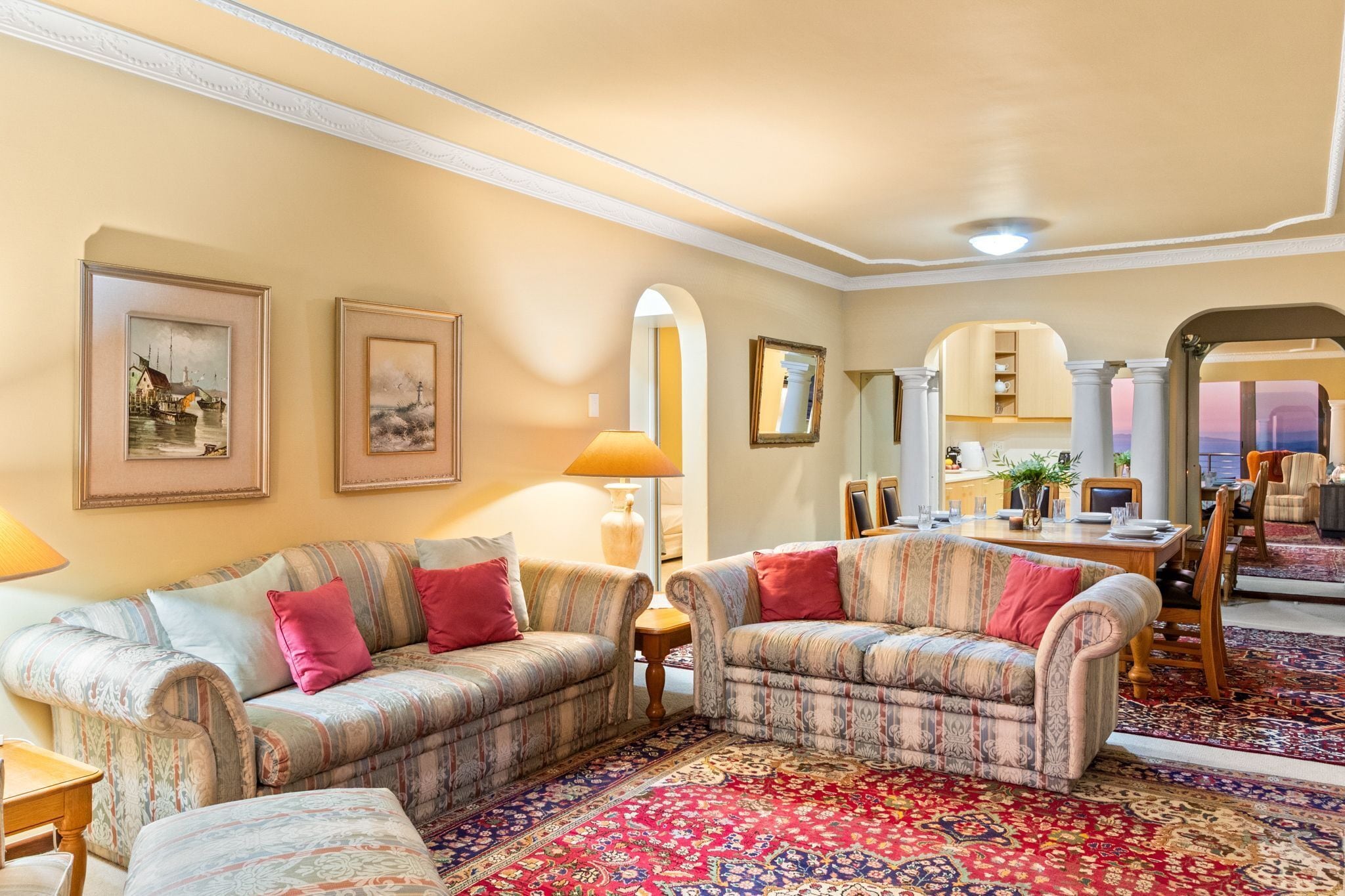 Ein Wohnzimmer mit zwei gemusterten Sofas, einem roten Teppich und gerahmten Kunstwerken an den Wänden.