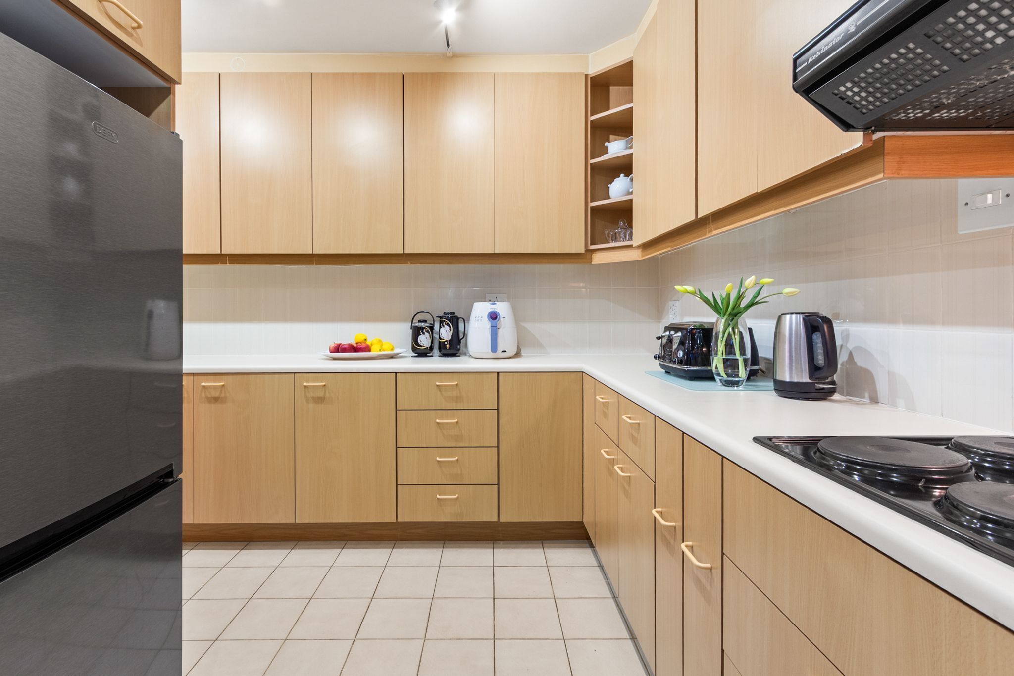 Una cocina moderna con armarios de madera, un refrigerador de acero inoxidable, una estufa y varios electrodomésticos sobre la encimera.