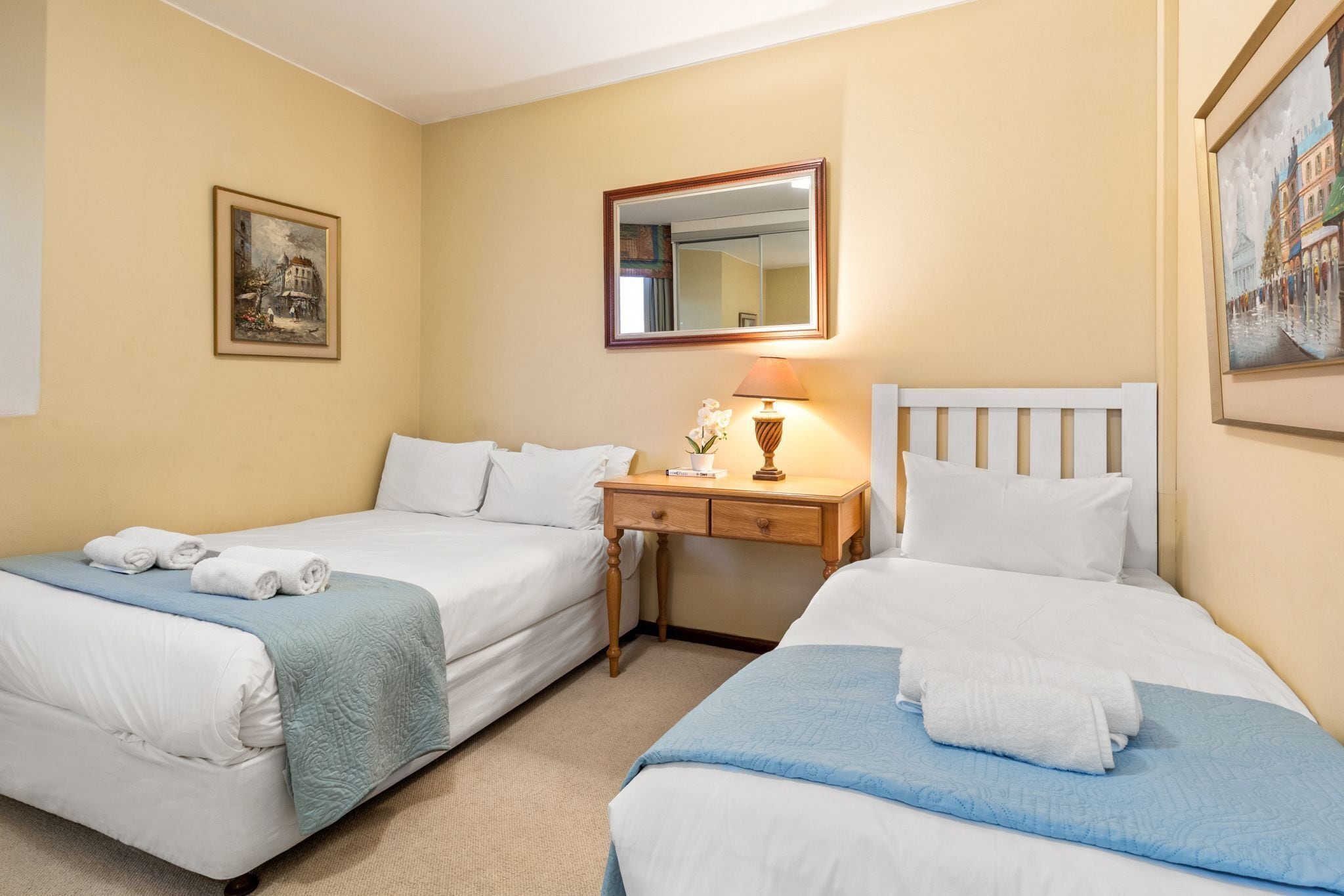 A hotel room with two beds, a nightstand, a lamp, and a painting on the wall.