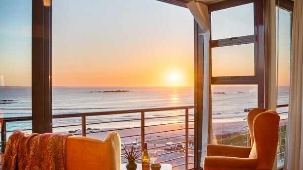 Ein Zimmer mit großem Fenster mit Blick auf einen Strand bei Sonnenuntergang.