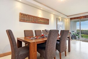 A dining area with a wooden table and six chairs, a decorative wall piece, and a view of the outdoors. - Dolphin Beach E5 (Cape Town)