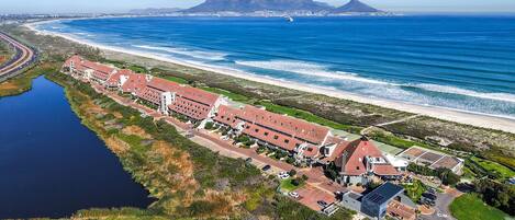 An aerial view of a coastal hotel with multiple buildings, a road, and a beach.