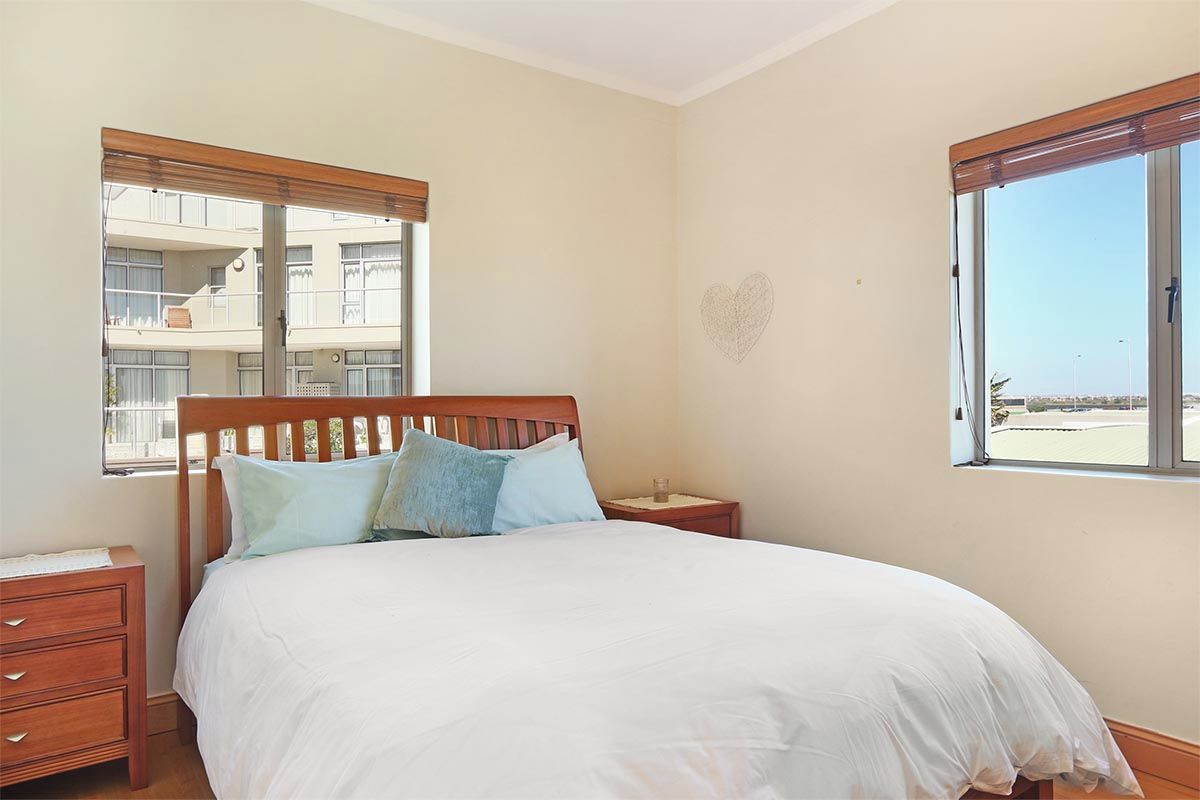 A bedroom with a wooden bed, a nightstand, a dresser, and a window with a view of a building.