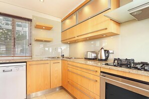 A modern kitchen with wooden cabinets, a stainless steel dishwasher, and a built-in oven. - Dolphin Beach E5 (Cape Town)
