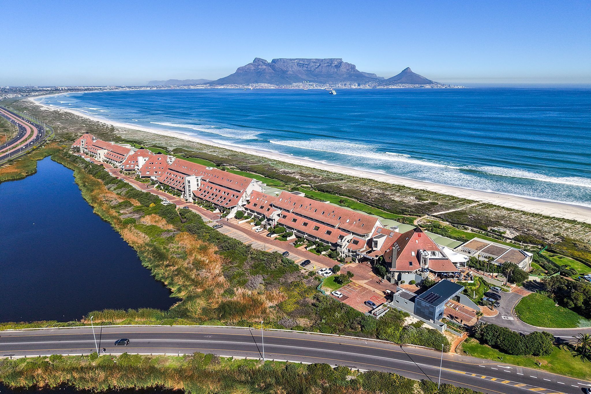 An aerial view of a coastal hotel with multiple buildings, a road, and a beach.