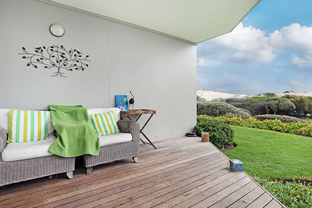 A covered outdoor seating area with a wicker sofa, striped cushions, and a small table.