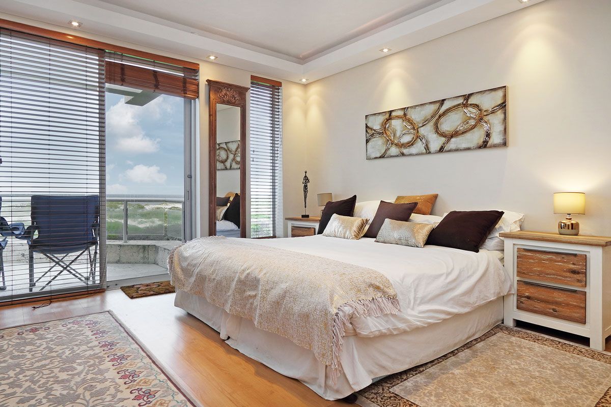 A spacious bedroom with a large bed, a balcony with a chair, and a view of the landscape.