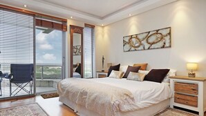 Une chambre spacieuse avec un grand lit, un balcon avec un fauteuil et une vue sur le paysage.