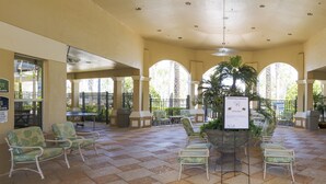 A covered outdoor seating area with tiled flooring, green patterned chairs, and a central planter. - Disney at Your Doorstep by VillaDirect (Kissimmee)
