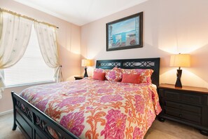 A bedroom with a bed, two bedside tables, a nightstand, a window with curtains, and a painting on the wall. - Disney at Your Doorstep by VillaDirect (Kissimmee)