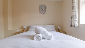 A neatly made bed with white linens and a rolled towel, two bedside lamps, and a framed picture on the wall. - Kynsparks Luxury Apartments (Birmingham)