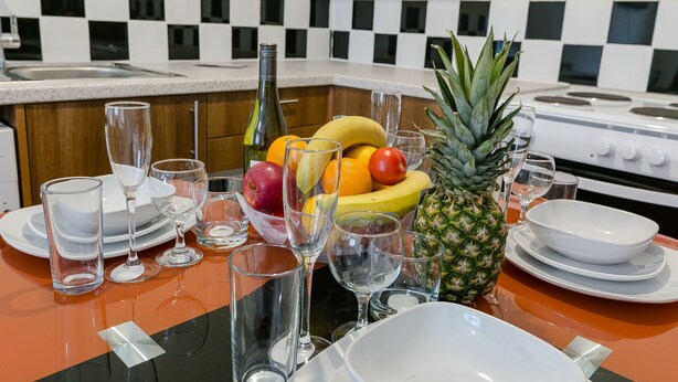 A kitchen with a checkered backsplash, a stove, and a fruit bowl with bananas, apples, oranges, and a pineapple. - Kynsparks Luxury Apartments (Birmingham)