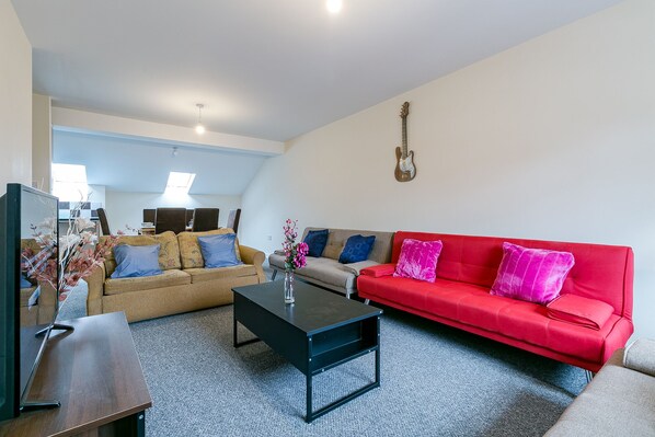 A living room with a red sofa, a beige sofa, a black coffee table, and a guitar on the wall.