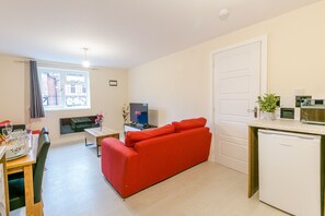 A compact living space with a red sofa, a dining table set with plates and glasses, a TV, and a kitchenette with a microwave and a coffee machine.