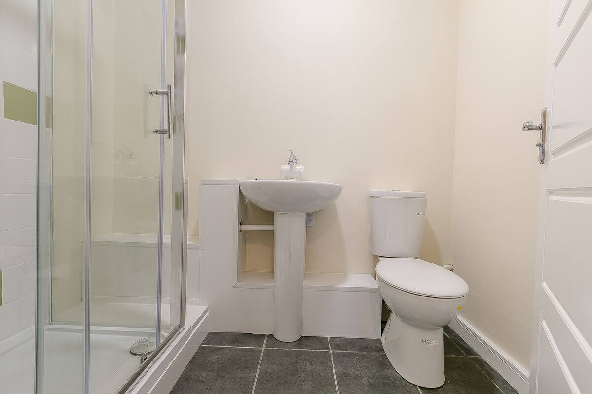 A small, clean bathroom with a glass shower enclosure, a pedestal sink, and a toilet.