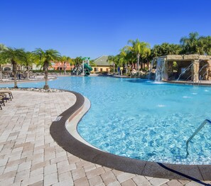 A large outdoor swimming pool with a waterfall feature, surrounded by palm trees and lounge chairs. - Princess Palms by VillaDirect (Kissimmee)