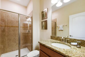 A bathroom with a glass-enclosed shower, a sink with a granite countertop, and a mirror above the sink. - Princess Palms by VillaDirect (Kissimmee)