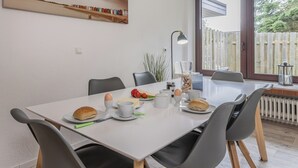 Une table à manger avec des aliments pour le petit-déjeuner, des chaises, une lampe et une fenêtre donnant sur une clôture.