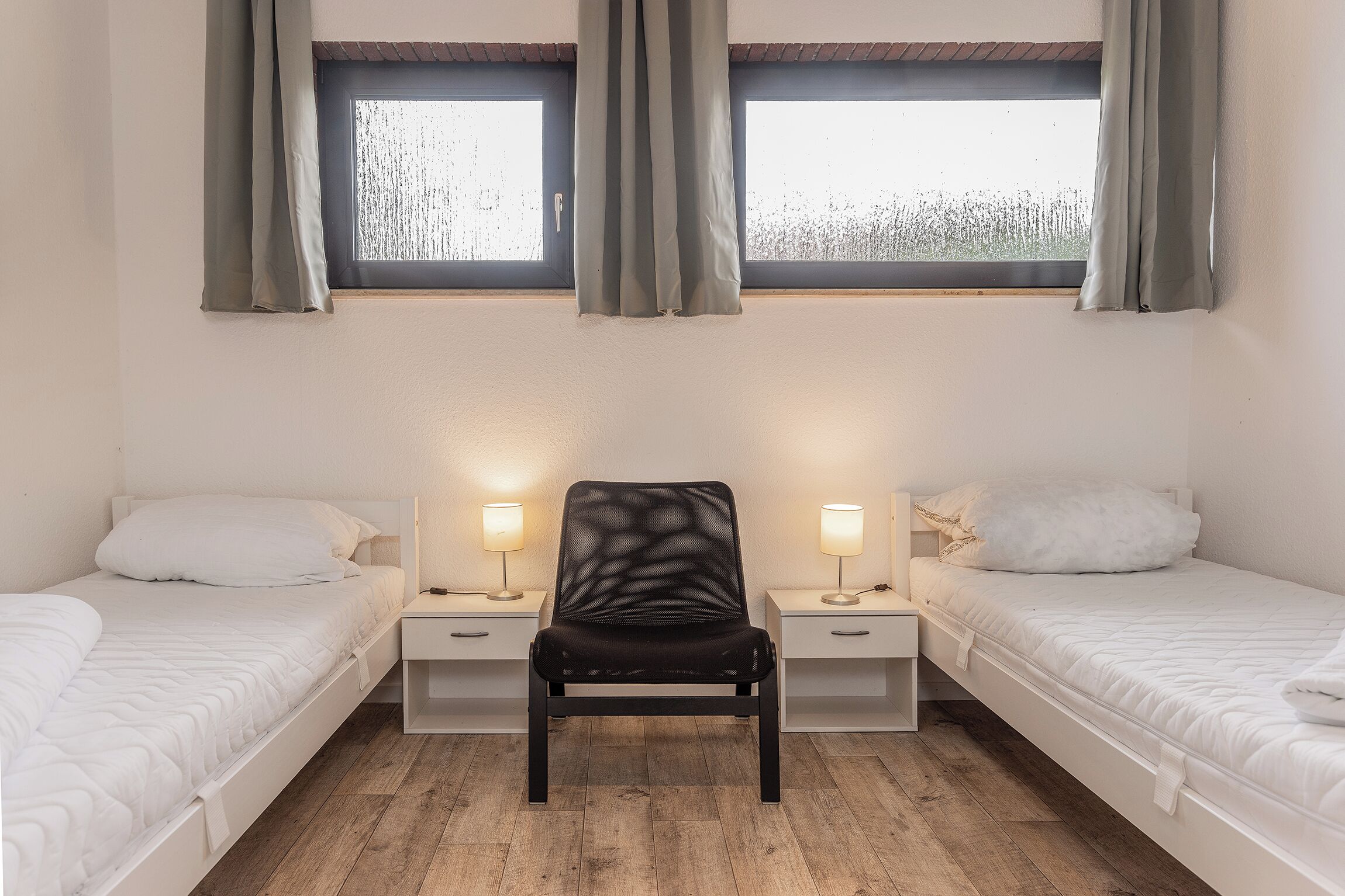 Een kamer met twee bedden, een stoel en twee nachtkastjes met lampen.