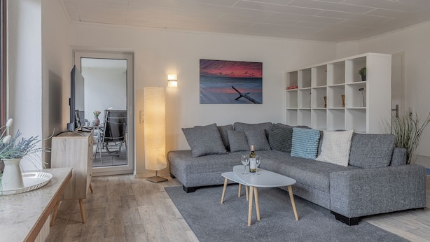 Un salon moderne avec un canapé gris, une table basse blanche et un tableau représentant un coucher de soleil.