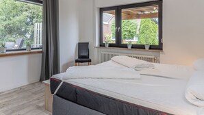 Une chambre à coucher avec un lit, une fenêtre avec des rideaux, un radiateur et une chaise.