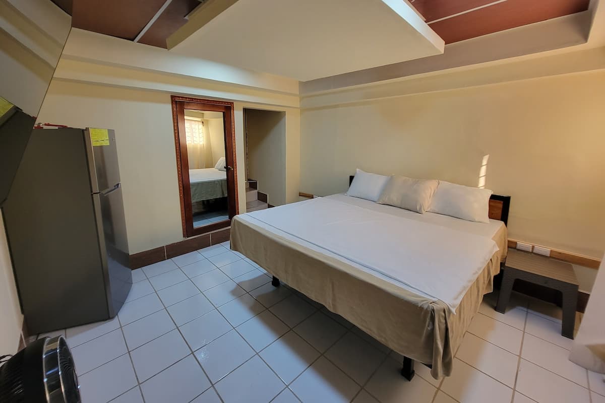 Quarto de hotel com cama, frigorífico, uma mesa pequena e escada para um andar superior.
