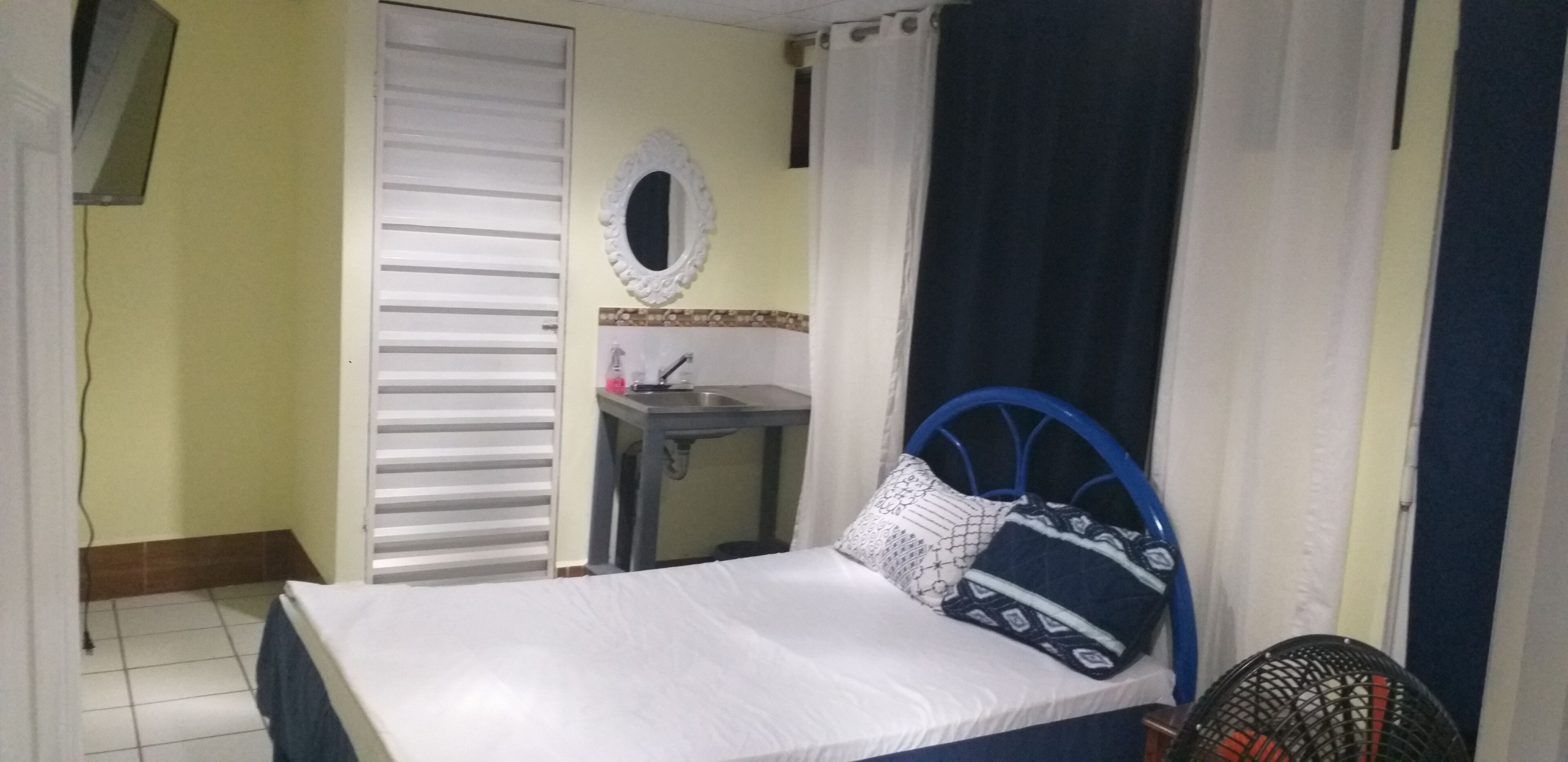 A bedroom with a bed, a bedside table, a mirror, and a window with curtains.