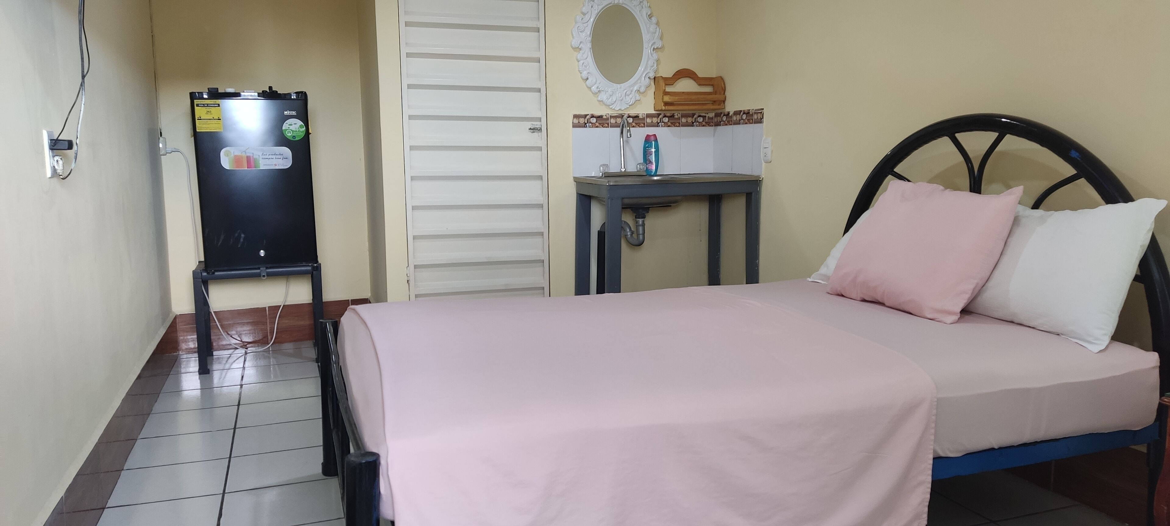 Ein Schlafzimmer mit einem Bett, einem kleinen Tisch mit Waschbecken, einem Kühlschrank und einer Tür.