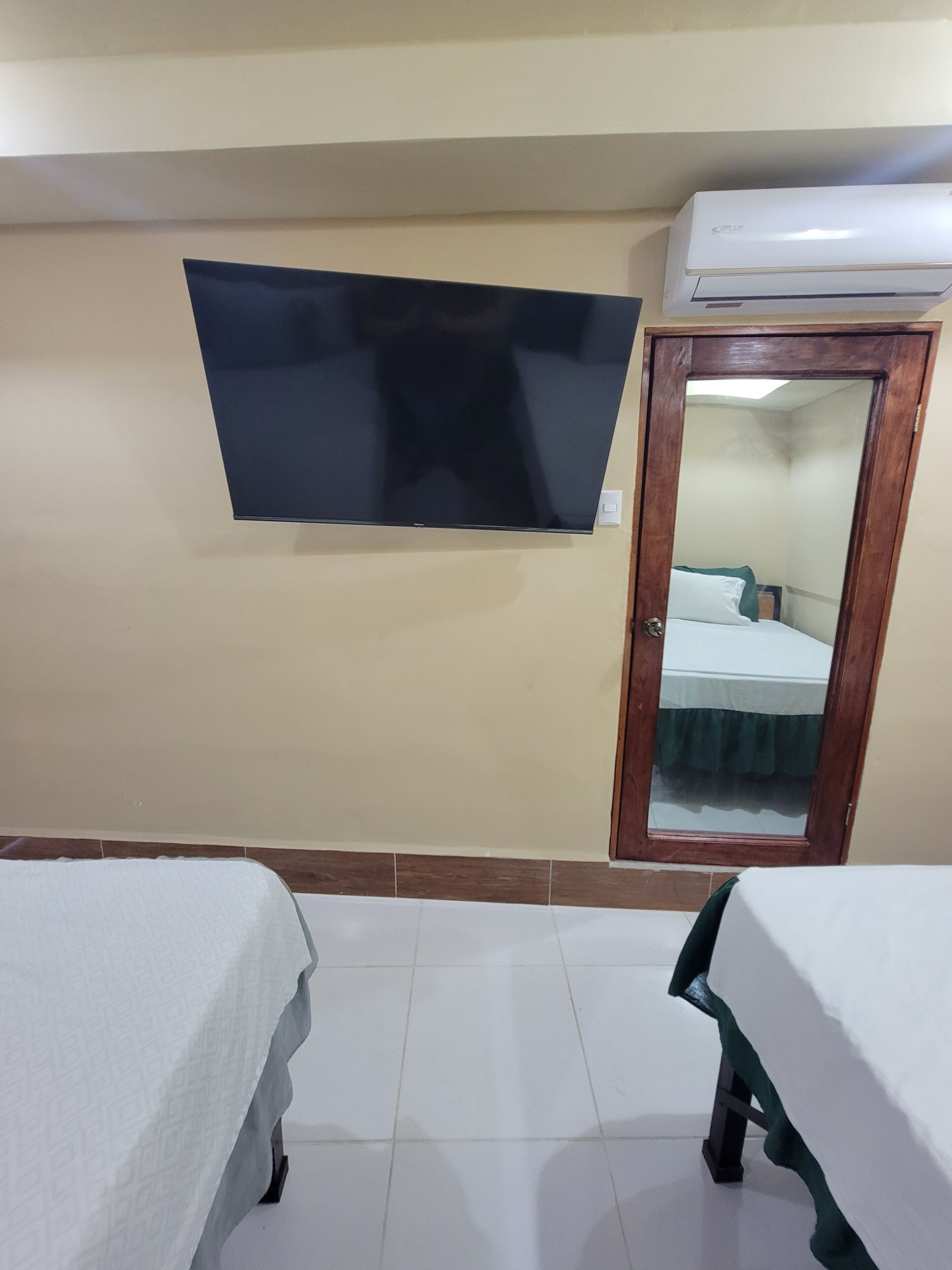 A hotel room with a bed, a TV mounted on the wall, and an air conditioning unit above the door.