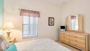 Un dormitorio con cama, cómoda, lámpara, ventana con persianas y un cuadro en la pared.