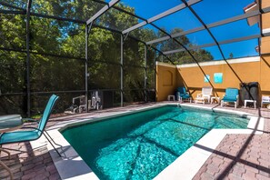 Una piscina con zona cubierta, sillas de descanso y patio de ladrillo.