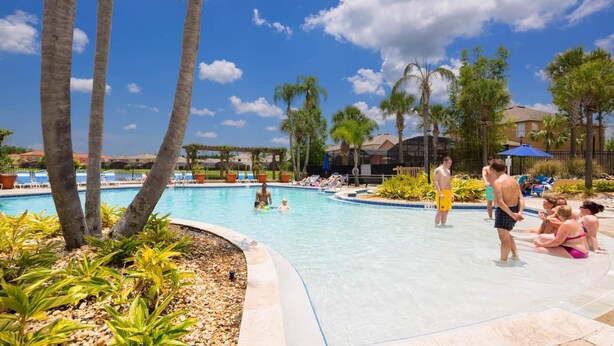 Zona de piscina con palmeras, sillas de descanso y un cielo azul despejado.
