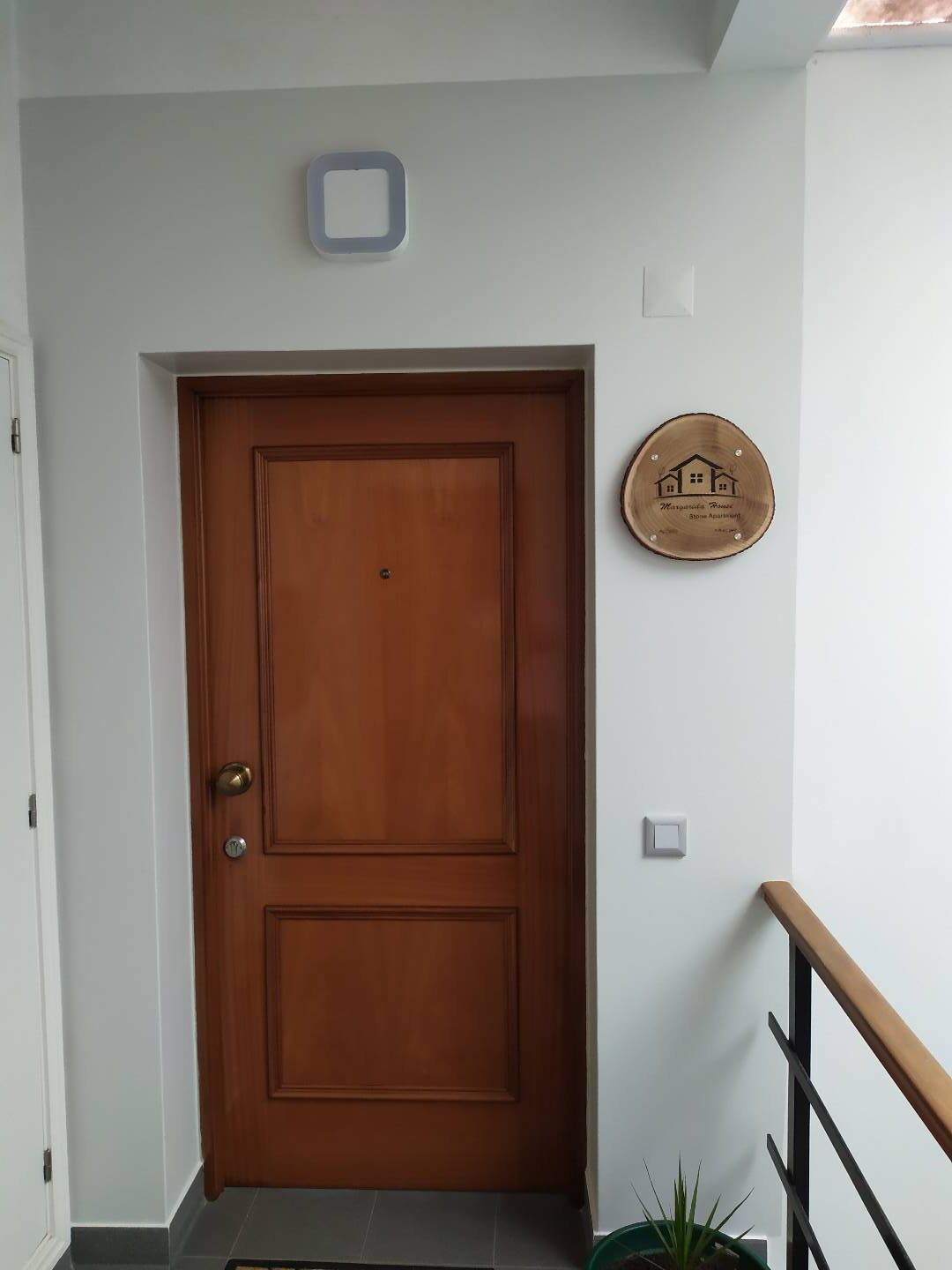 Une porte en bois avec une poignée de porte en laiton, une petite plaque fixée au mur et un escalier avec une rampe en bois.