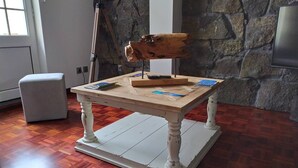 Una pequeña mesa de madera con un diseño rústico, ubicada en una habitación con pared de piedra y suelo de madera.