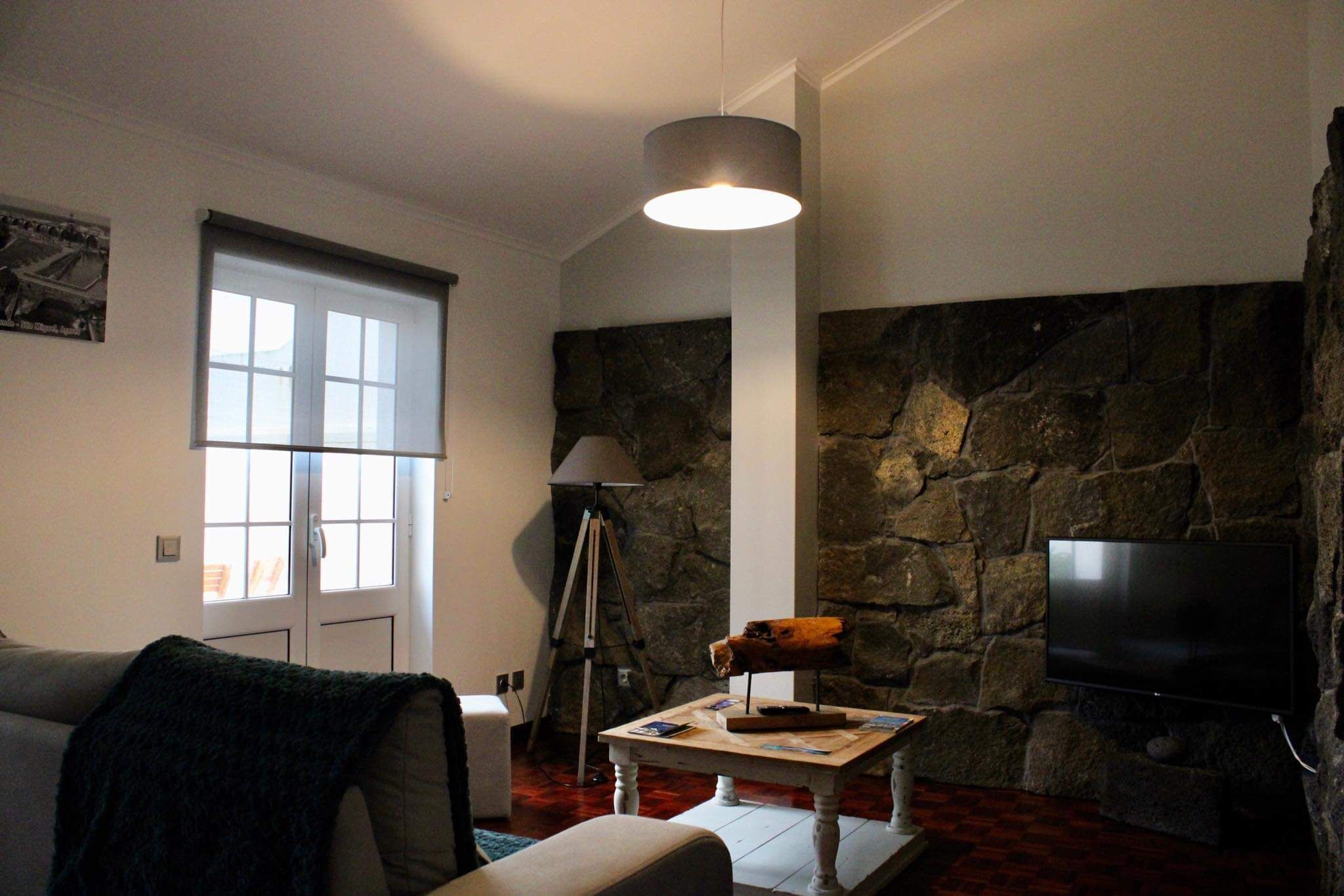 A living room with a stone wall, a television, a lamp, and a window with blinds.
