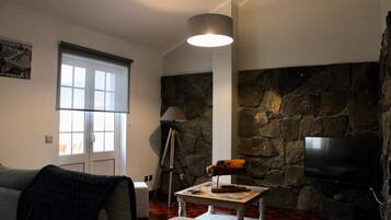 A living room with a stone wall, a television, a lamp, and a window with blinds.