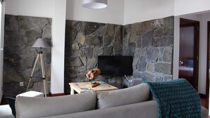 Una sala de estar con pared de piedra, televisor montado, un trípode y un sofá acogedor.