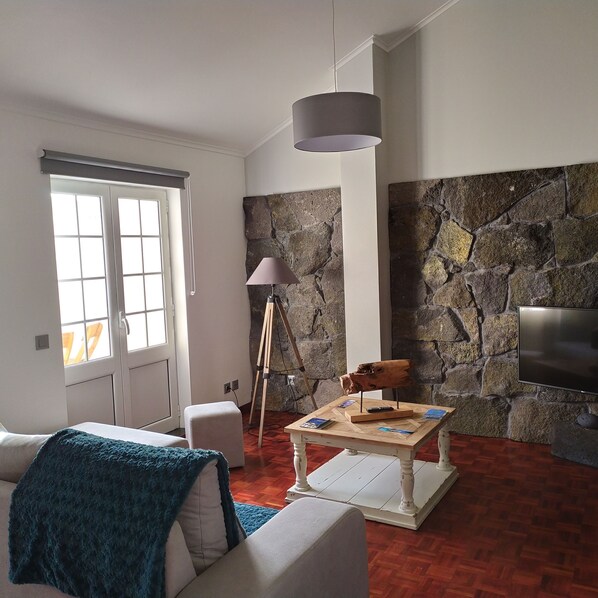Un salon avec un mur en pierre, un canapé blanc, une lampe et un téléviseur.