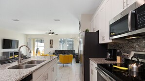 Een moderne keuken met granieten aanrechtbladen, roestvrijstalen apparatuur en een eethoek met gele stoelen.