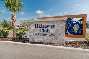 A sign for the Hideaway Club at Storey Lake, featuring a stone facade and a decorative palm tree mural. - Fairy Tales by VillaDirect (Kissimmee)