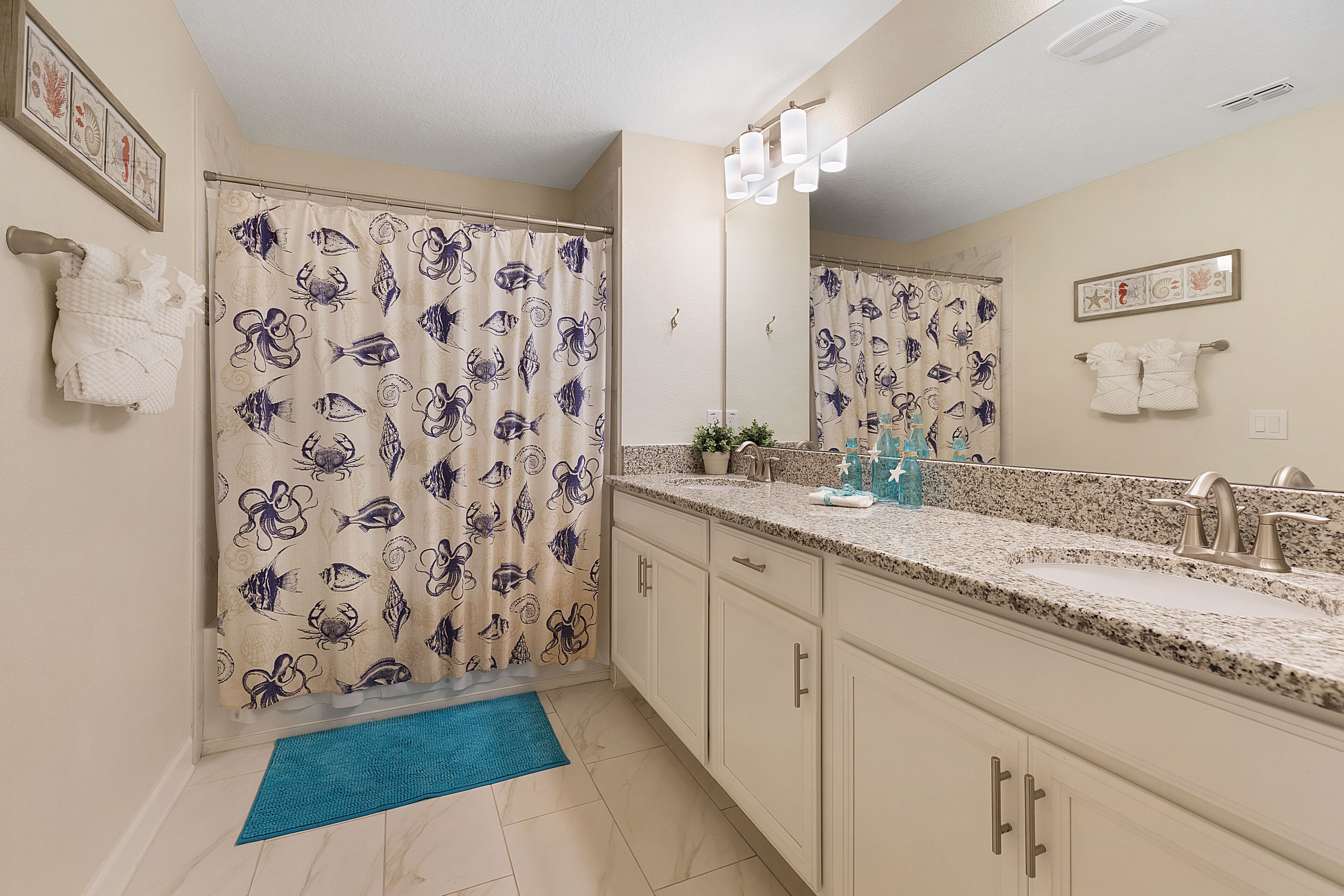 A bathroom with a shower curtain featuring a fish pattern, a sink with a granite countertop, and a mirror above the sink.