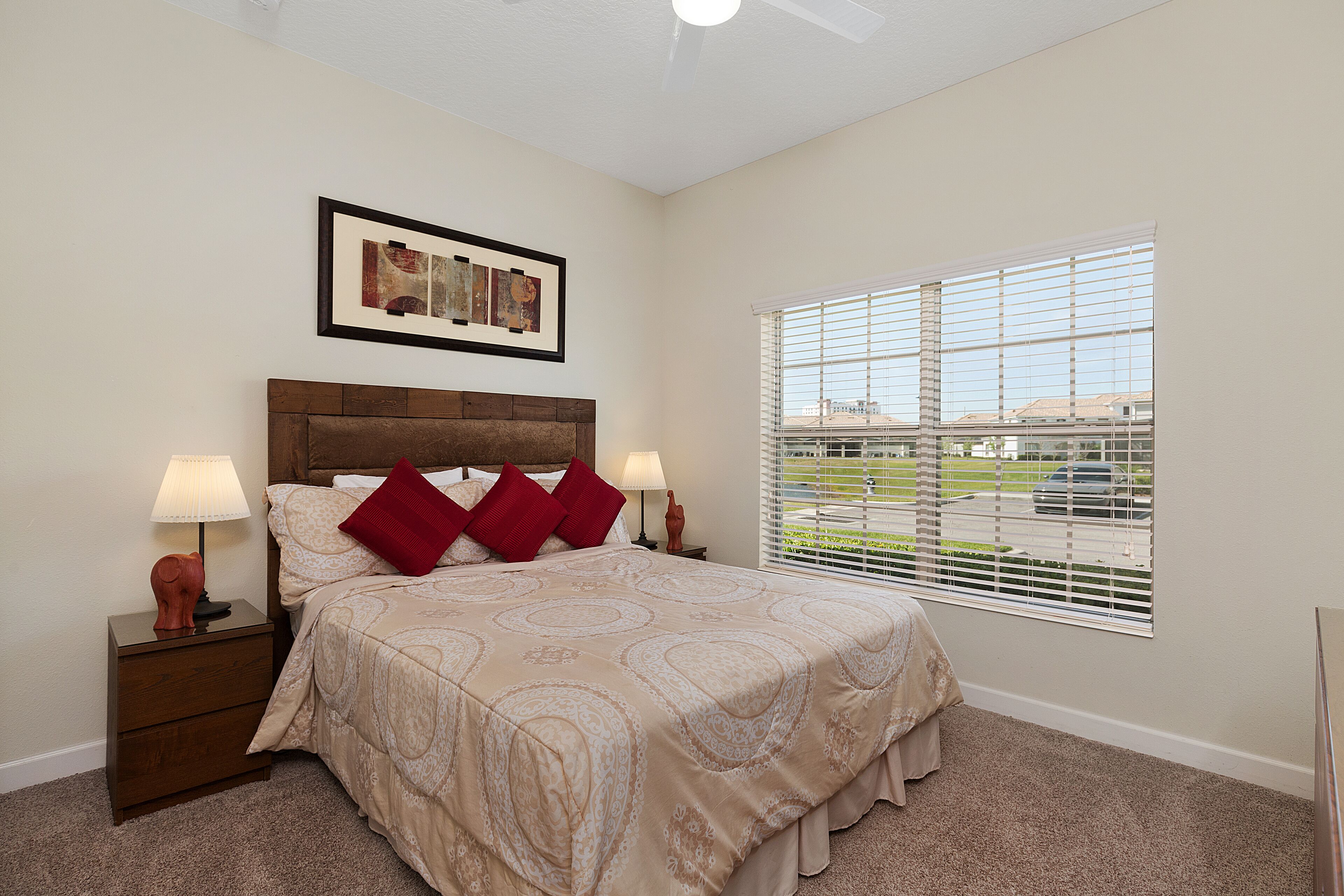 A bedroom with a large bed, two nightstands, a ceiling fan, a window with blinds, and a framed picture on the wall.