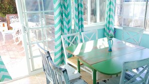 A conservatory with a glass door, white chairs, a wooden table, and a vase with flowers.