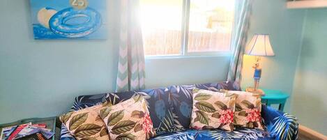 A room with a blue sofa, floral cushions, a window with curtains, a lamp, and a wall with a 'Float Rentals' sign.