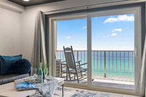 Un balcon avec vue sur l’océan, une chaise et une table avec une bouteille et des verres.