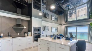 Una cocina moderna con armarios blancos, una isla central y vistas al mar a través de amplios ventanales.