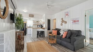 Ein modernes Wohnzimmer mit einem grauen Sofa, einem kleinen Couchtisch und einer Küche im Hintergrund.