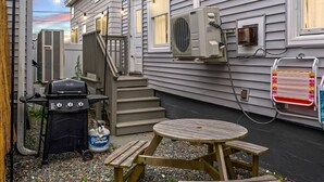 Ein Garten mit Grill, einem Klapptisch und einer an der Hauswand befestigten Klimaanlage.