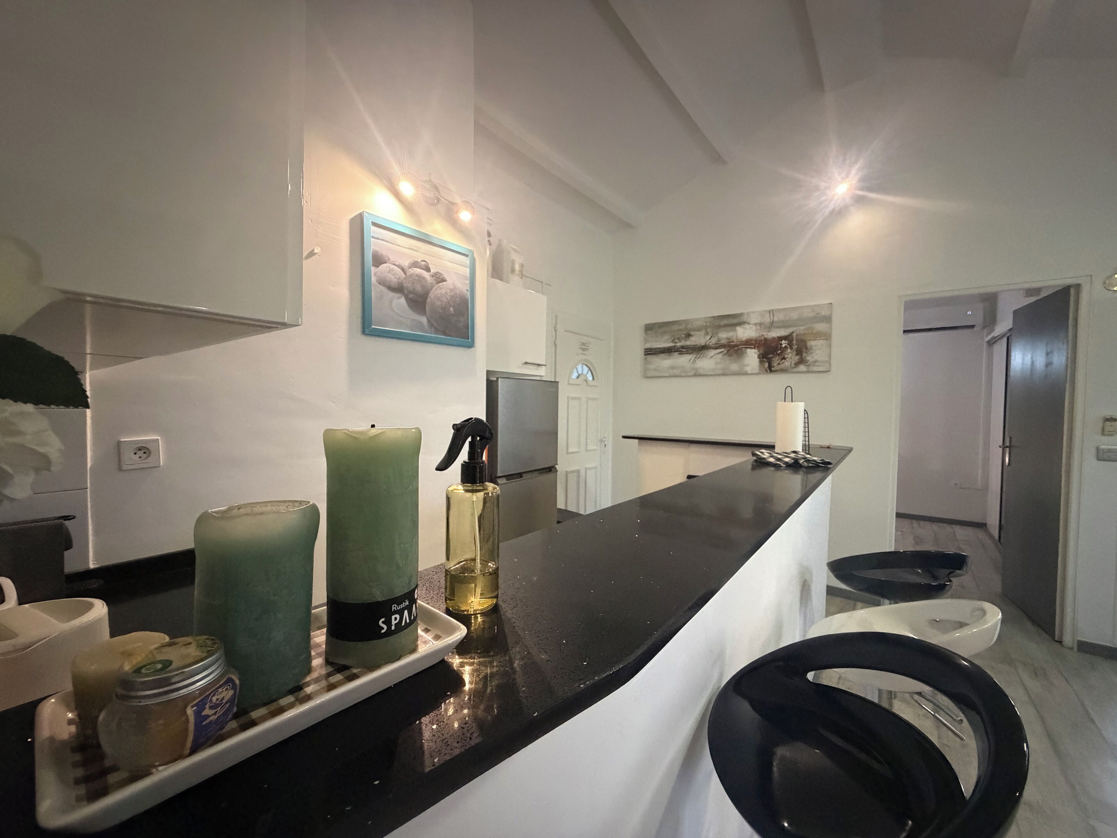 Cocina moderna con encimera negra, una vela verde, un pulverizador y un frasco de mermelada.
